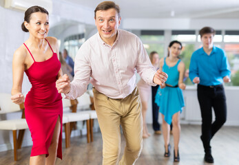 Fototapeta premium Group is of different ages active people engaged in Latin dance studio and learns movements of cha-cha-cha dance