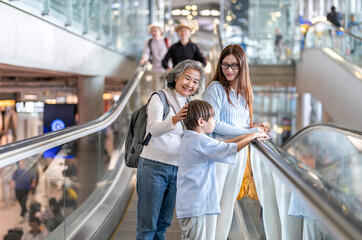 Asian family traveler on airport escalator, grandmother smiling with grandson, mother beside them...