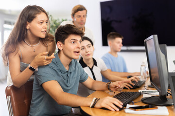 Group of cheerful enthusiastic young developers engaged in IT startup, gathered around desk in...