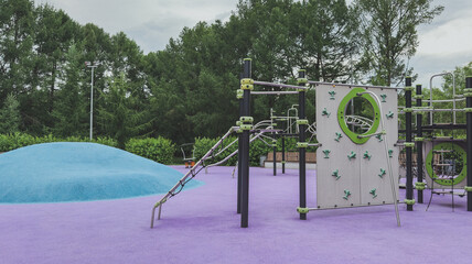 Colorful modern playground with climbing walls, rope structures and a blue hill on a vibrant purple surface, surrounded by greenery, concept of childhood fun and physical development