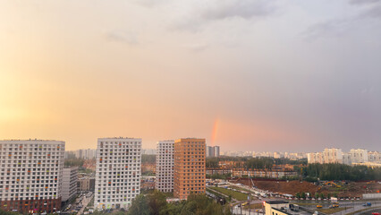 Urban cityscape with high-rise buildings, construction site and rainbow at sunset, concept of urban development and weather contrast