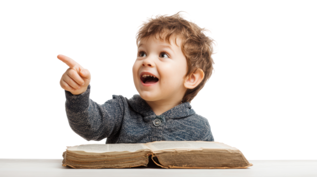 A joyful child pointing and smiling while sitting at a table with a book.