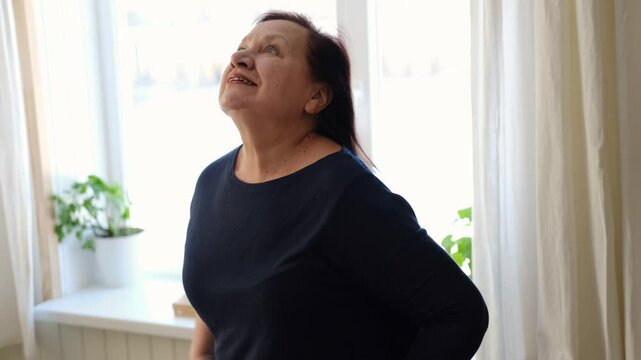Senior woman dance at home. Elderly lady listening song and moving. Old female brunette feels calmly, relish carefree retired life looks happy. Vitality, wellness. Grandmother dancing alone indoors.