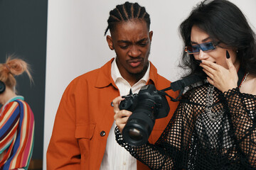 Young adult man and woman coworkers socializing while reviewing camera content in a modern workplace, reflecting Gen Z business and work culture atmosphere.