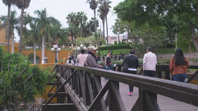 Tourists crossing wooden bridge in barranco district of lima, peru, with yellow church in background