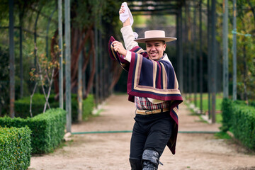 Portrait of a smiling, cheerful young man dressed as a Chilean huaso, celebrating and posing to...