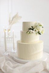 Delicious wedding cake with floral decor and burning candles on table indoors