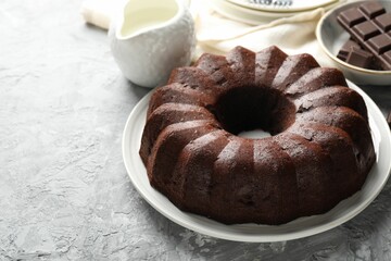 Tasty bundt cake, pieces of chocolate and milk on grey table, closeup. Space for text