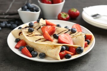 Tasty crepes with strawberries, blueberries and chocolate sauce on gray textured table, closeup