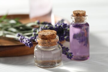 Natural essential oil and lavender flowers on white wooden table, closeup