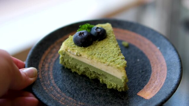 Green cake slice, Matcha cheesecake blueberries, slice ofcheesecake is shown on a wooden table. slice is cut in half and is being held up by a knife. Concept of indulgence and enjoyment. High quality
