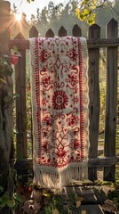 embroidered Ukrainian rushnyk towel, rustic wooden fence, outdoor scene, realistic style, golden sunlight, vivid red and white tones, rule of thirds with towel on right
