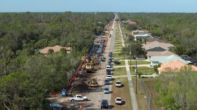 Florida residential street with active roadworks and closed lane. Cars drive cautiously through narrowed path controlled by temporary traffic lights.