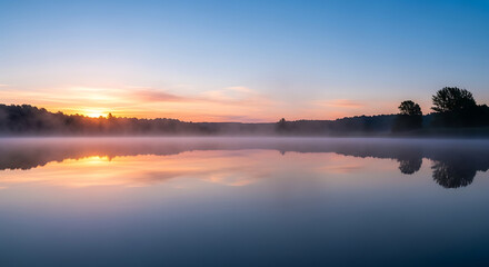 Fototapeta premium Serene lake reflecting a clear sky at dawn, mist rising from the water