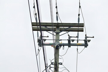 Close-up of a utility pole with multiple power lines and insulators against a cloudy sky.