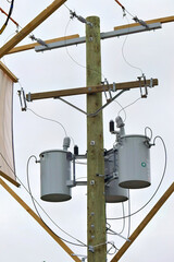 Electrical transformers mounted on a wooden utility pole against a cloudy sky.
