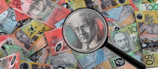 Magnifying glass inspecting a pile of australian dollar banknotes, focusing on the fifty dollar bill.