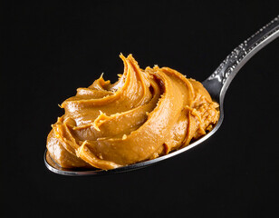 Close-up of a spoon holding smooth nut butter against a dark background