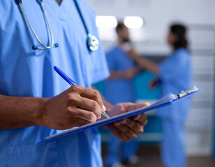 Healthcare worker in blue scrubs writing on a clipboard with stethoscope in bright medical environment