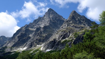 Majestic mountain peaks under a clear blue sky with scattered clouds, surrounded by lush green foliage and patches of snow.