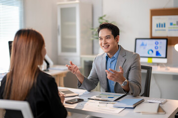 A man and a woman are sitting at a desk, talking to each other
