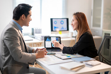 A man and a woman are sitting at a desk with a laptop and a monitor