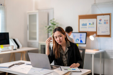 Obraz premium A woman is sitting at a desk with a laptop and a stack of papers