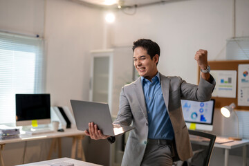 A man in a suit is holding a laptop and smiling