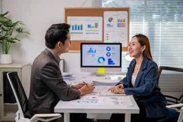 Two people are sitting at a desk with a computer monitor in front of them