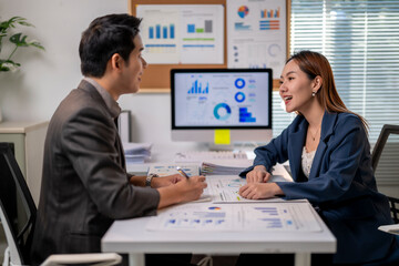 Two people are sitting at a desk with a computer monitor in front of them