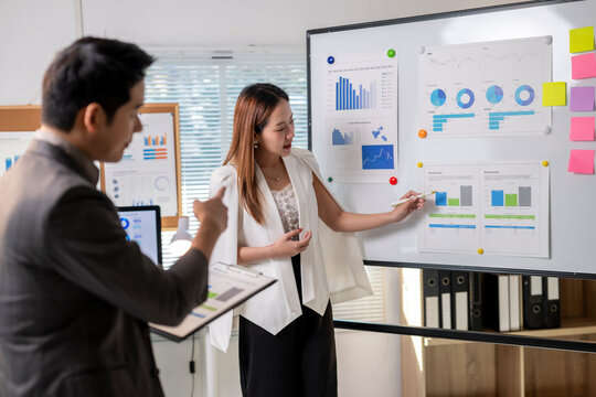 A man and a woman are standing in front of a white board with graphs and charts - Powered by Adobe
