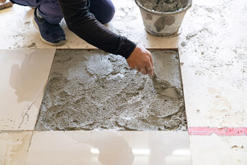 The worker is applying mortar to the tile installation area using a trowel.
