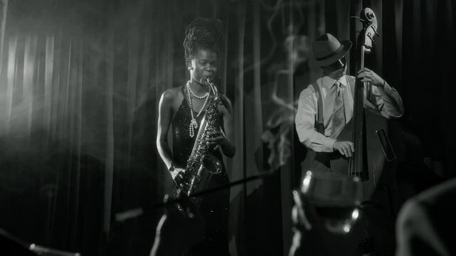 Black and white shot of glamorous Black woman playing saophone on stage while performing as duo in vintage jazz club with cigarette smoke