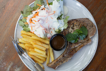 Black pepper pork steak with french fries and vegetable salad on a white plate