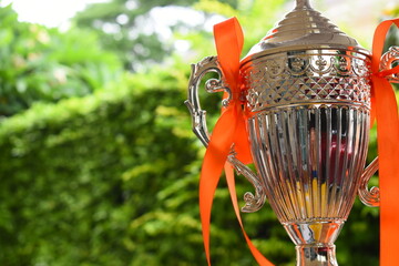 beautiful golden trophy with orange ribbon on green tree background
