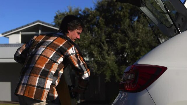 Man in Plaid  Shirt loading Yellow Suitcase from Car Trunk