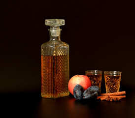 Plum-apple liqueur with spices on a black background, a crystal decanter and two glasses of...