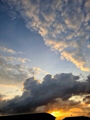 Obraz premium Layered sky with blue tones, golden sunrise clouds, and dark thick cloud above orange horizon with house silhouettes, capturing dramatic early morning scene.