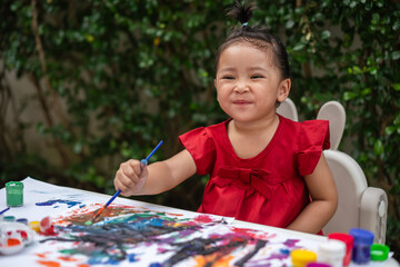 happy toddler girl painting watercolor in paper at backyard.
