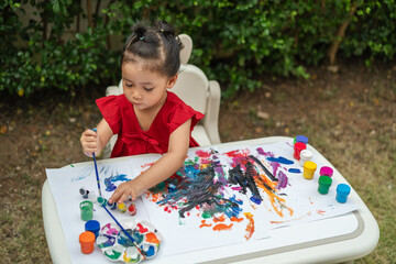 happy toddler girl painting watercolor in paper at backyard.