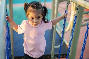 happy toddler girl playing and walking on wooden rope bridge at a outdoor playground in park