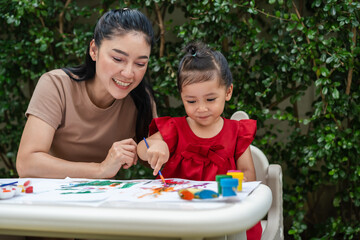 happy mother and toddler girl painting watercolor in paper at backyard.