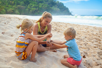 Happy kids with mother have fun on white sand beach. Couple of children playing with mother. Travel lifestyle, swimming activities in family summer camp. Vacations on tropical island.