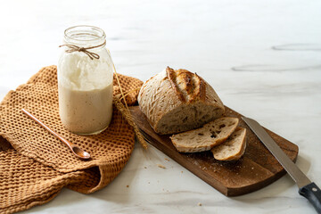 Crispy sourdough bread sits beside a glass jar filled with active starter, accompanied by a rustic...