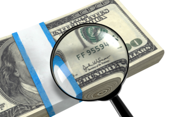 Magnifying glass inspecting the serial number on a stack of one hundred us dollar bills on a transparent background.