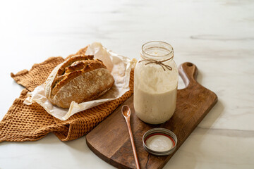Crispy sourdough bread sits beside a glass jar filled with active starter, accompanied by a rustic...