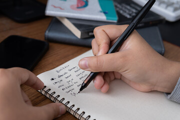 Close-up photograph of a hand writing notes in a spiral notebook a concept for journaling studying...