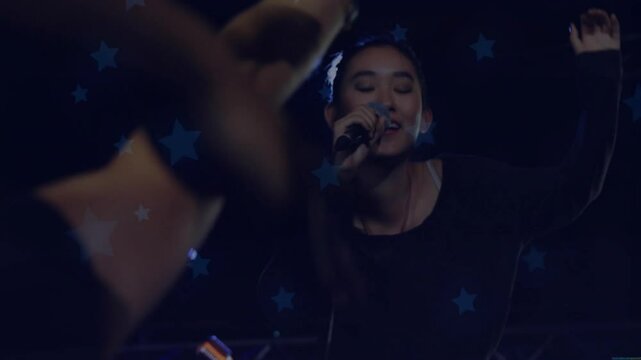 Closing eyes and gripping microphone, singer starting music while fans reaching under star lights