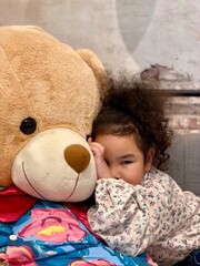 Little girl lying on the floor with a big teddy bear.