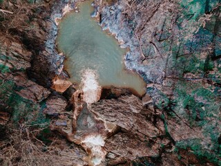 Aerial view of a waterfall cascading into a pool surrounded by rocks and trees. The water flows...